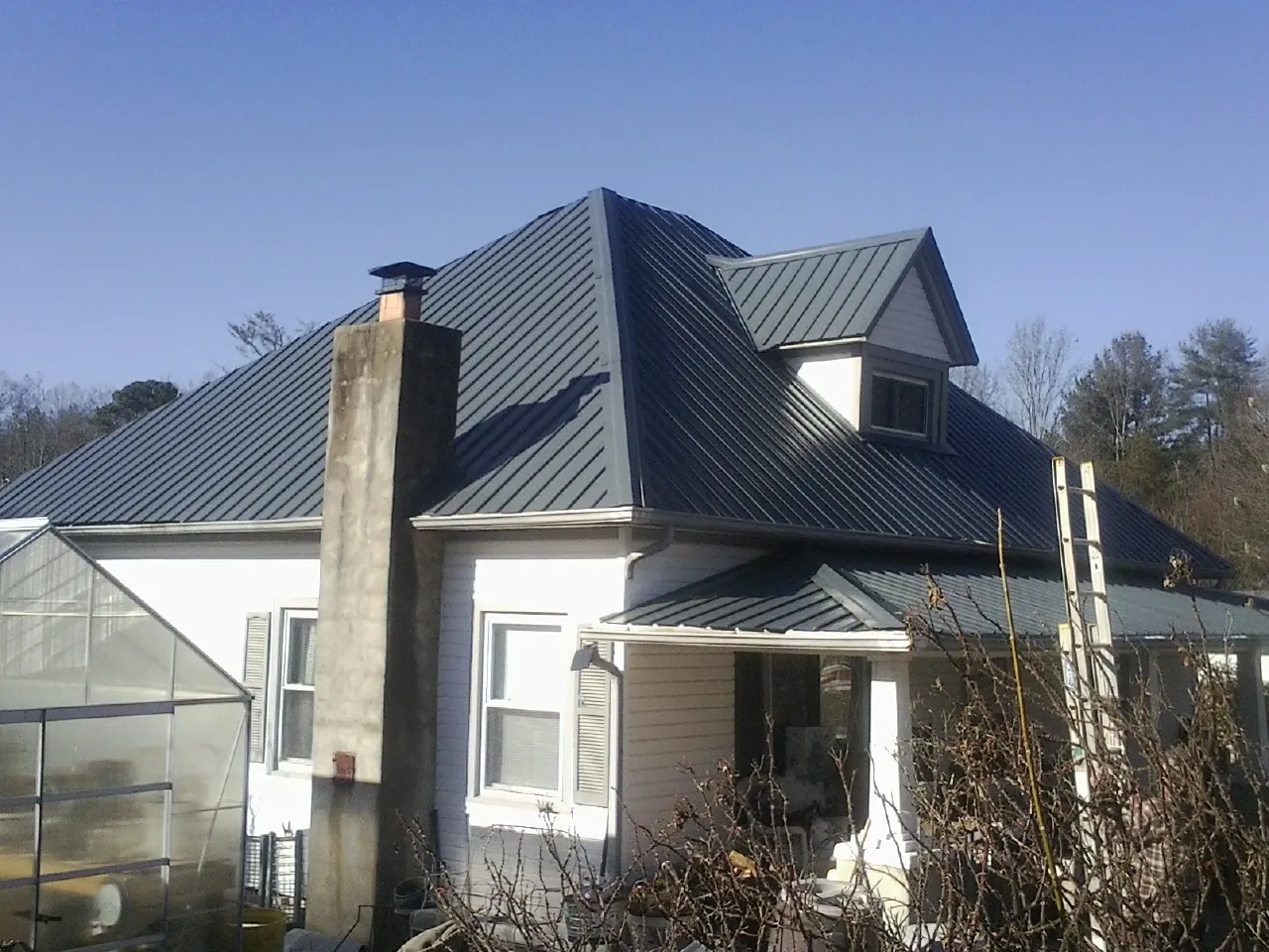 Dark blue standing seam metal roof on a white farmhouse with dormer — Slate & Tile Roof Repair by Roofing Brothers in Hadley