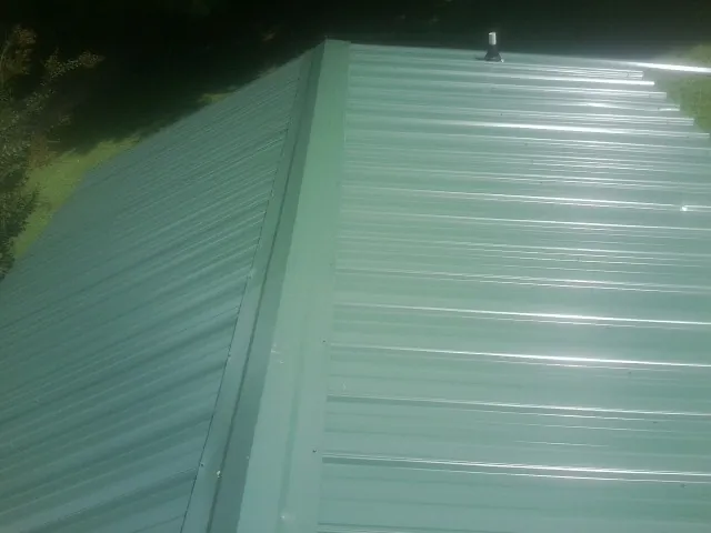 New green metal panels meeting at the ridge of a roof — Flat Roof Repair work by our crew in Hadley